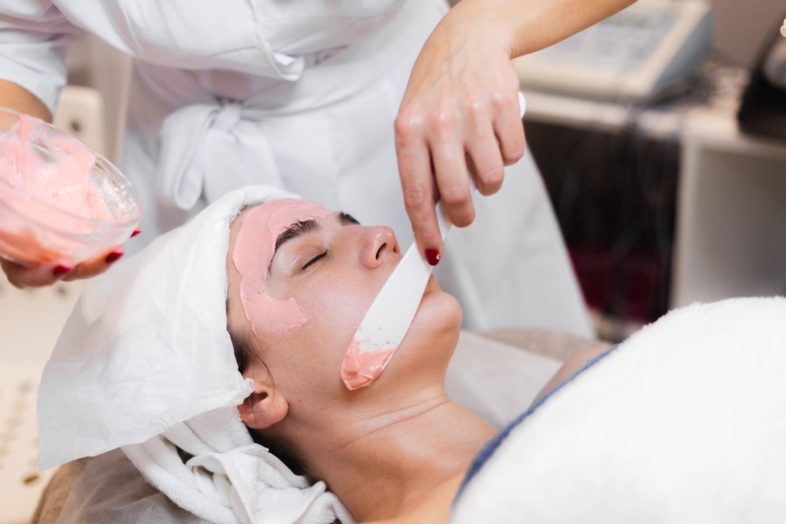 cosmetologist applies alginate mask with spatula on a woman's face