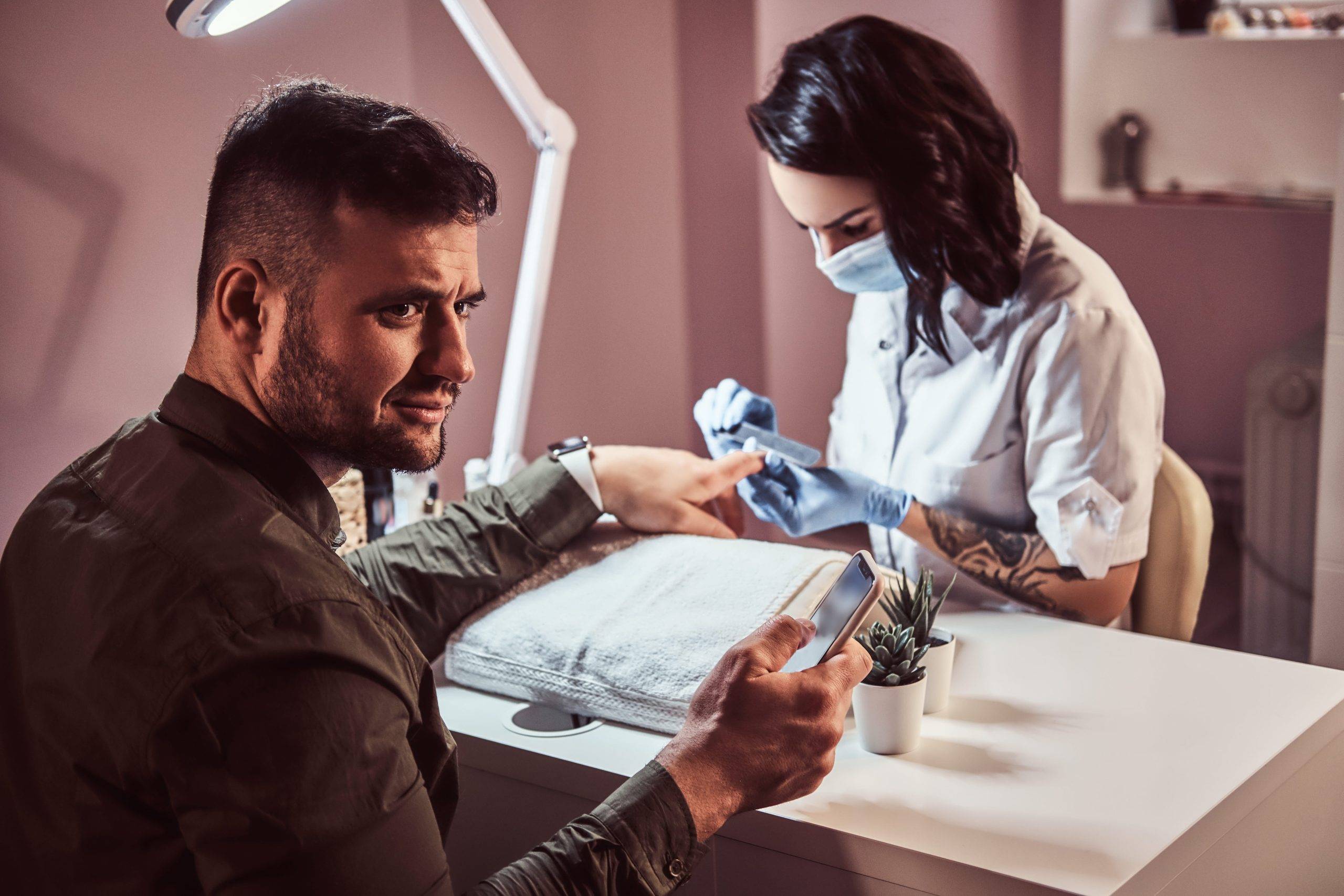 A man receiving manicure by beautician in a beauty salon